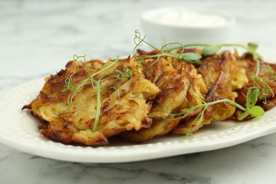 Photo of Delicious potato pancakes with fresh microgreens on white marble table, closeup