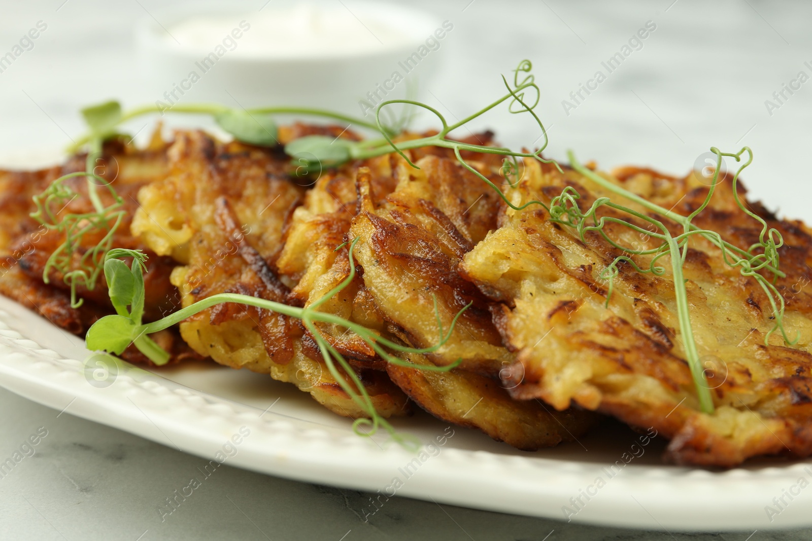 Photo of Delicious potato pancakes with fresh microgreens on white marble table, closeup