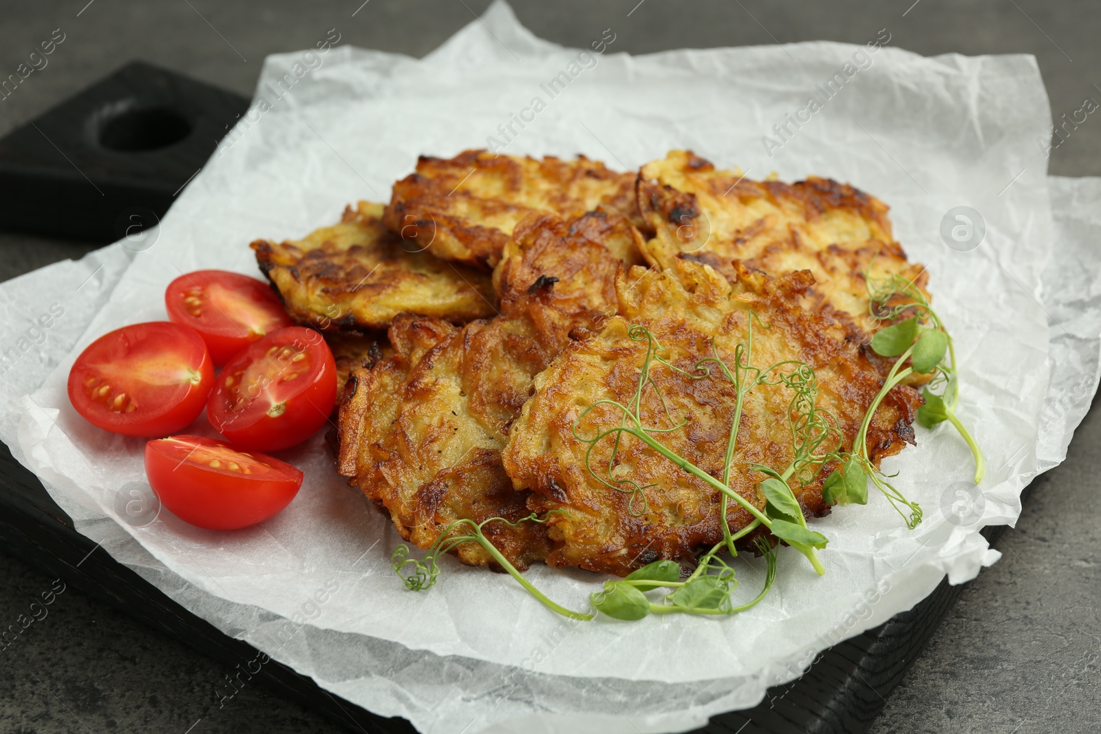 Photo of Delicious potato pancakes with fresh tomatoes and microgreens on grey table, closeup