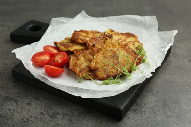 Photo of Delicious potato pancakes with fresh tomatoes and microgreens on grey table, closeup