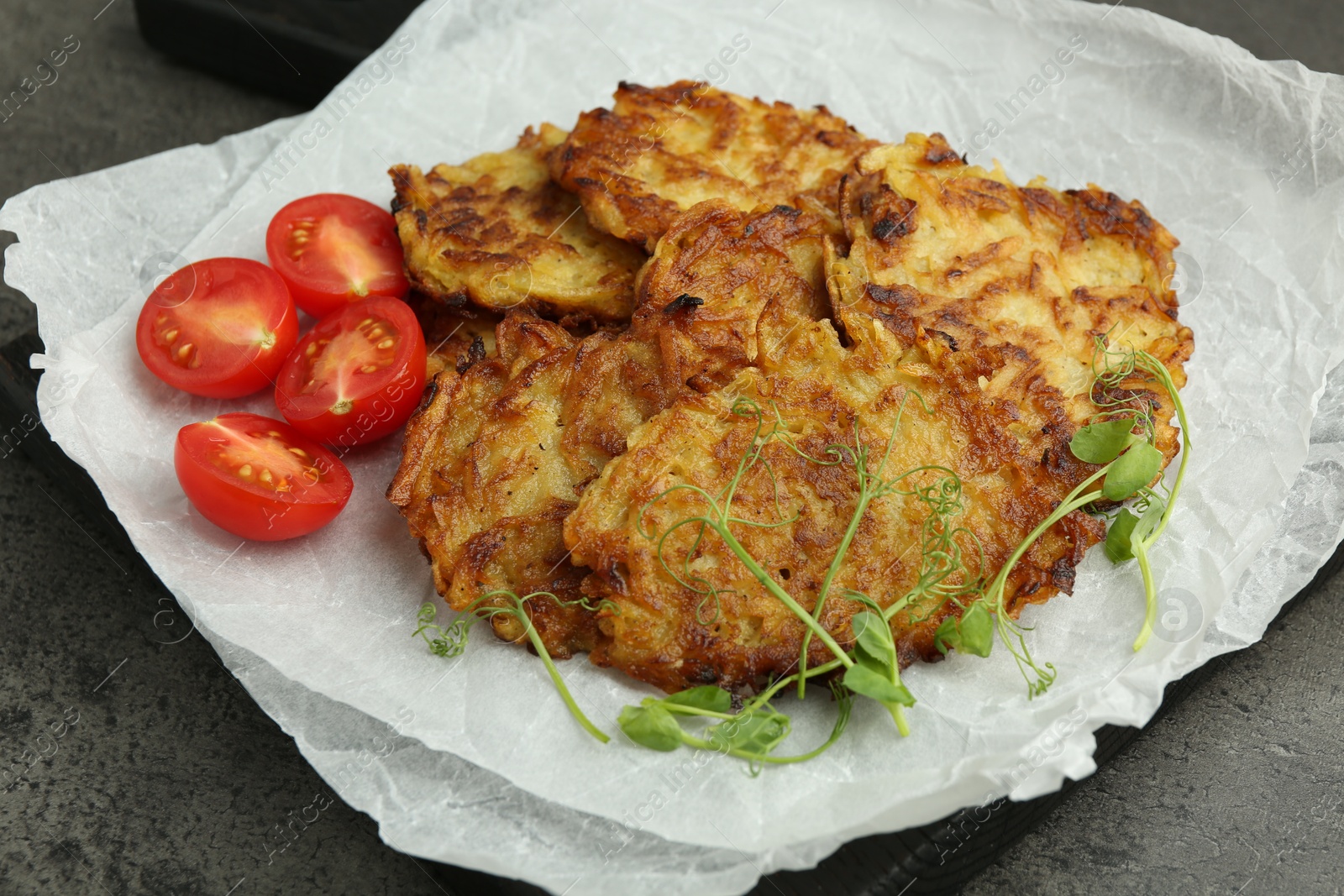 Photo of Delicious potato pancakes with fresh tomatoes and microgreens on grey table, closeup