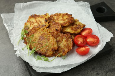 Photo of Delicious potato pancakes with fresh tomatoes and microgreens on grey table