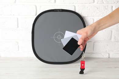 Photo of Woman with white balance calibration cards at wooden table, closeup