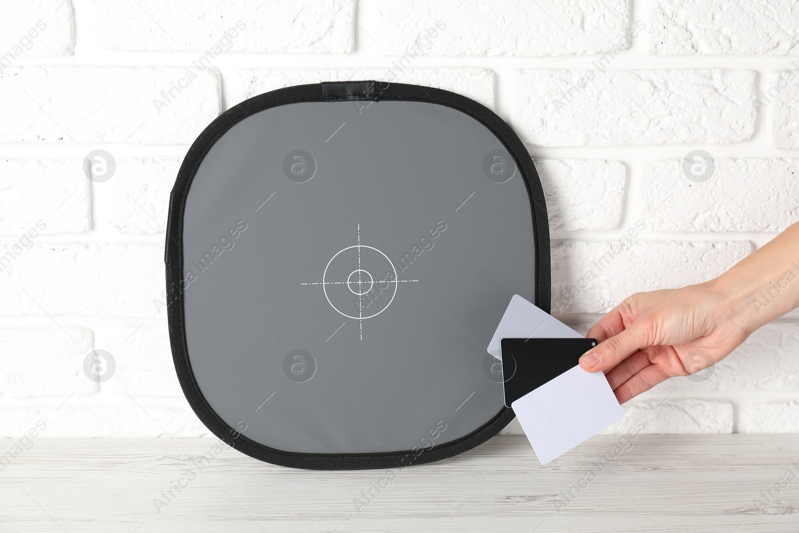 Photo of Woman with white balance calibration cards at wooden table, closeup