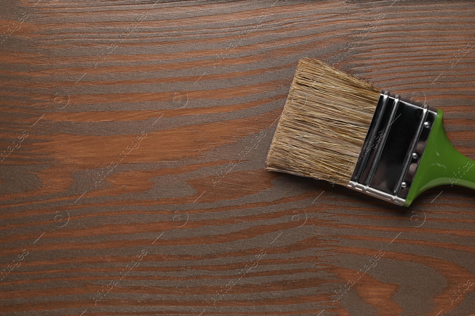 Photo of Applying walnut wood stain. Brush on wooden surface, top view. Space for text