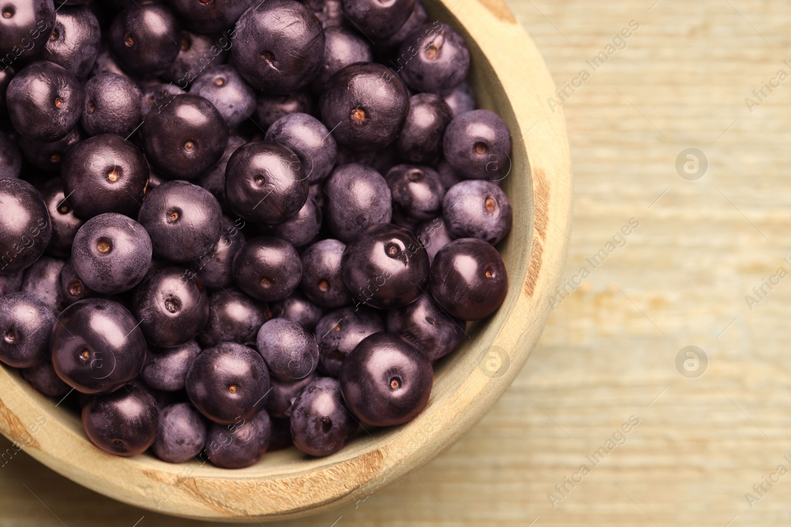 Photo of Ripe acai berries in bowl on wooden table, top view. Space for text