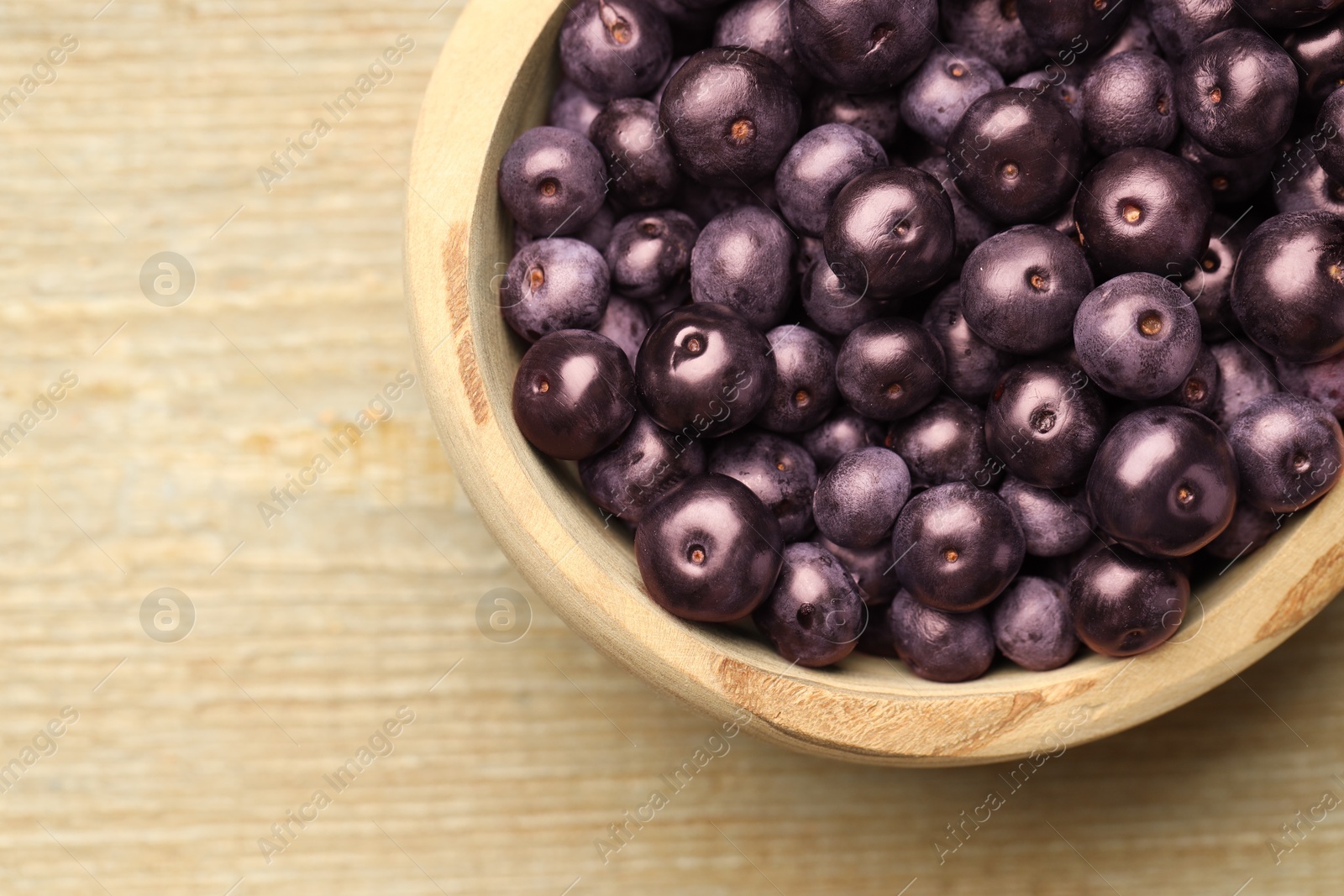 Photo of Ripe acai berries in bowl on wooden table, top view. Space for text