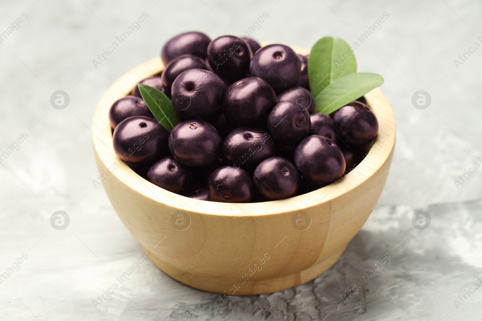 Photo of Ripe acai berries and leaves in bowl on grey textured table, closeup