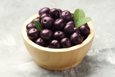 Ripe acai berries and leaves in bowl on grey textured table, closeup