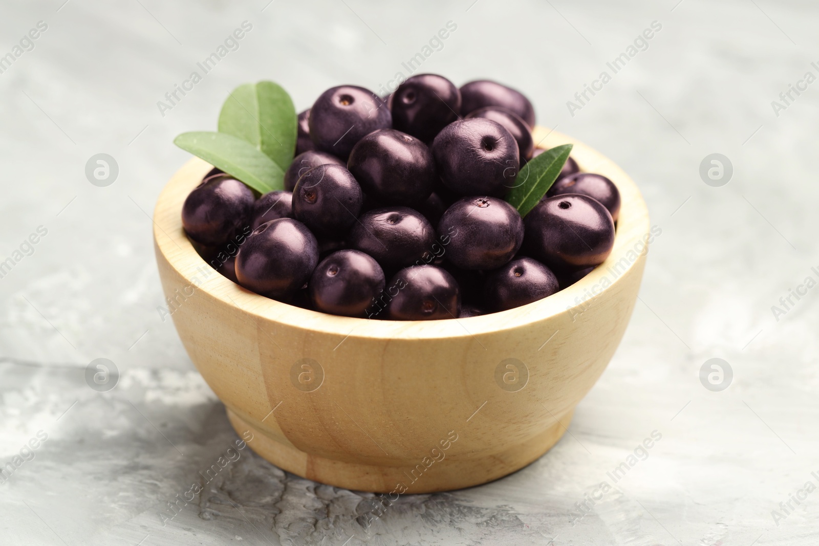 Photo of Ripe acai berries and leaves in bowl on grey textured table, closeup