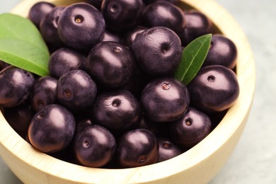 Photo of Ripe acai berries and leaves in bowl on table, closeup