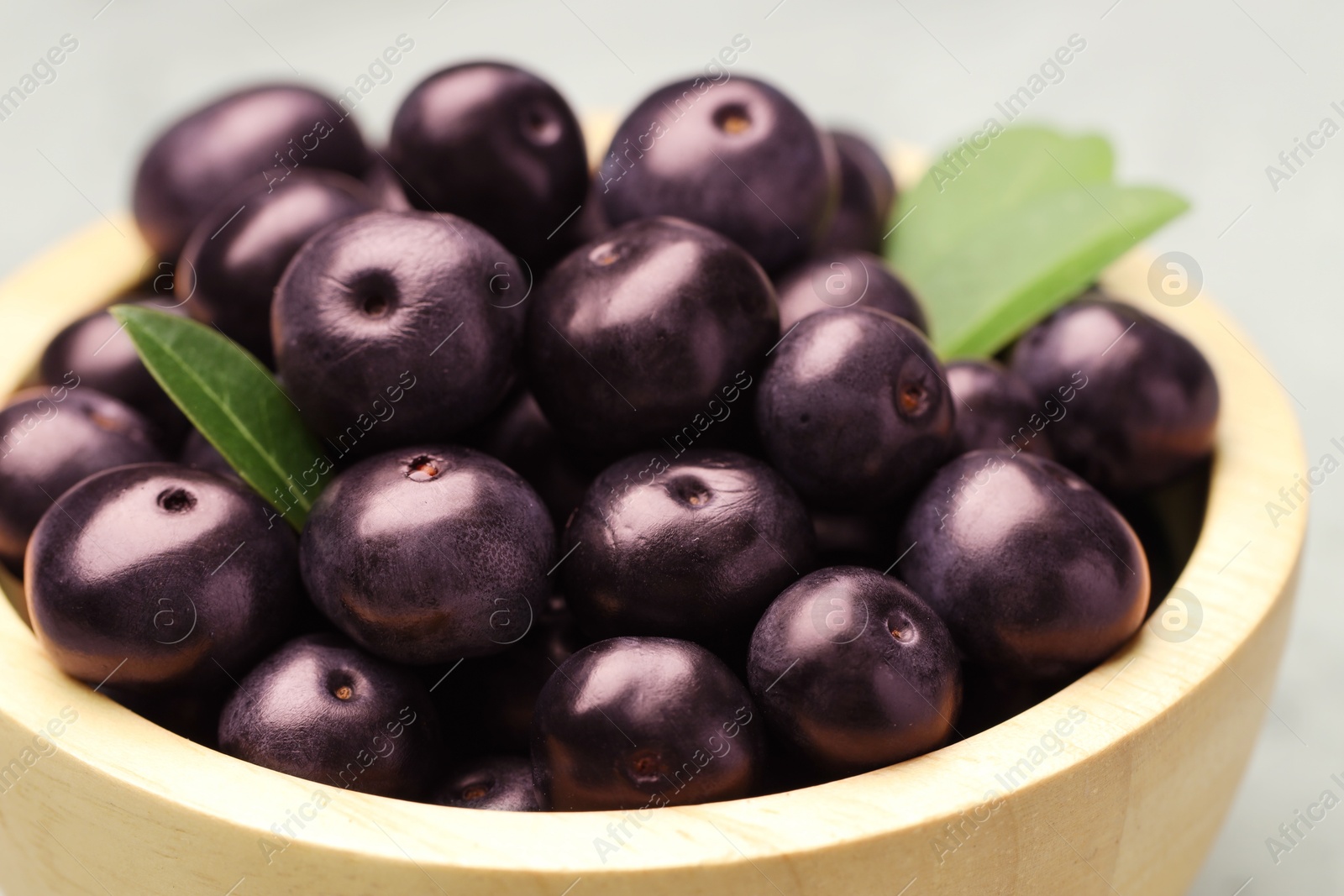 Photo of Ripe acai berries and leaves in bowl on table, closeup