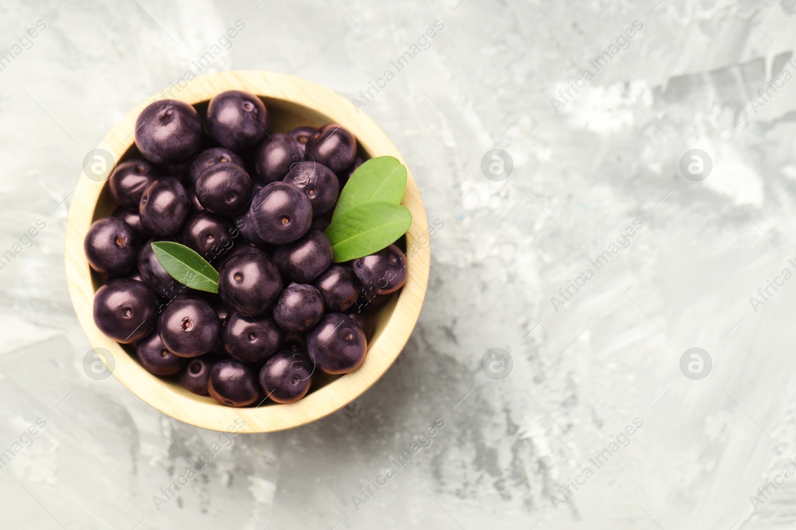 Photo of Ripe acai berries and leaves in bowl on grey textured table, top view. Space for text