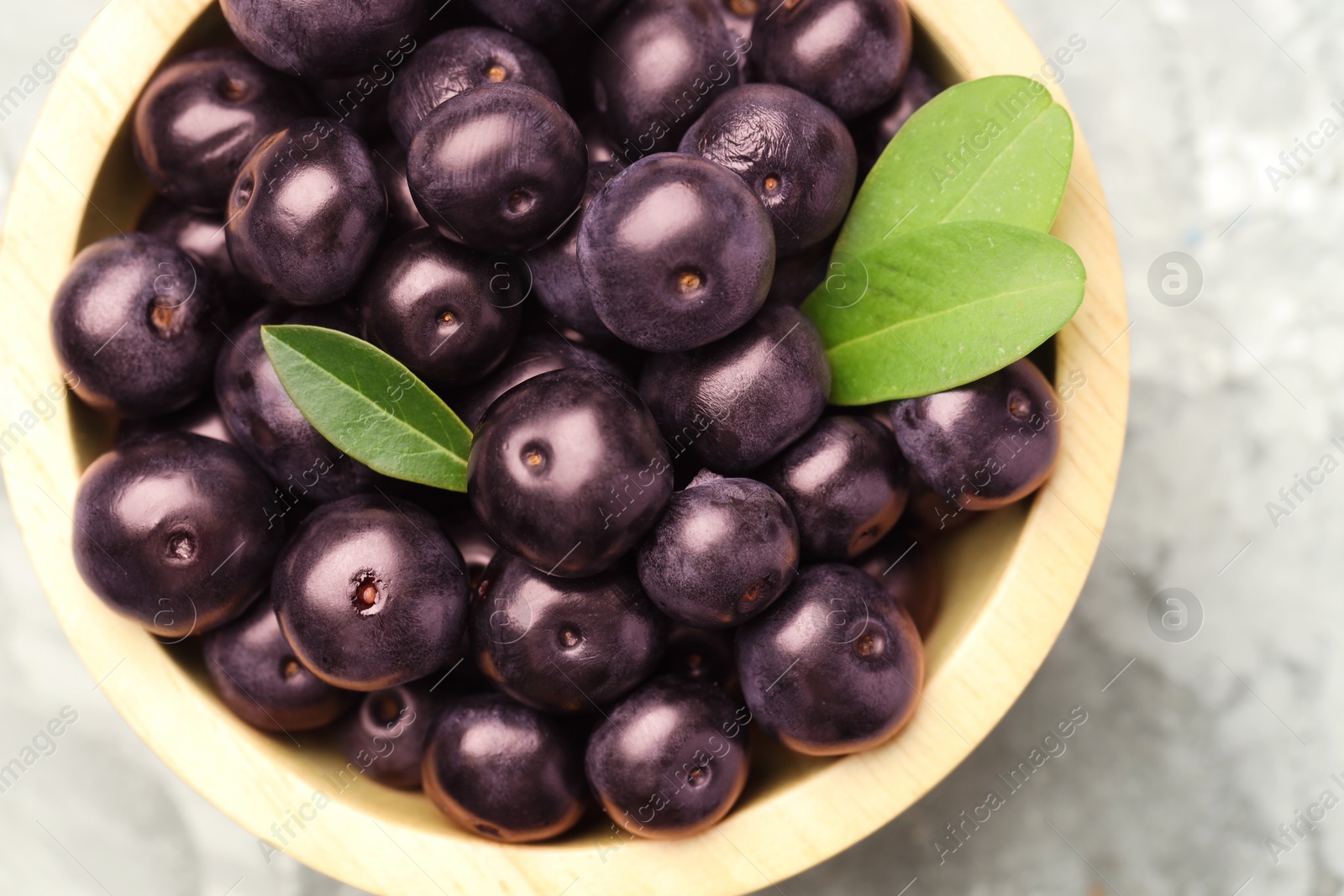 Photo of Ripe acai berries and leaves in bowl on grey table, top view