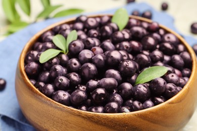 Photo of Ripe acai berries and leaves in bowl on table, closeup