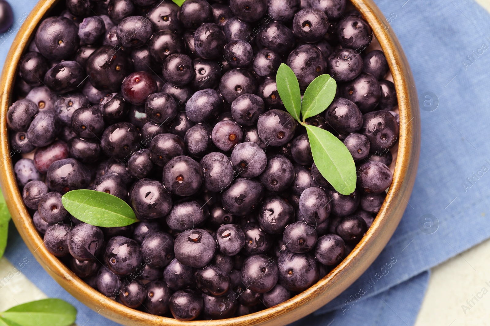 Photo of Ripe acai berries and leaves in bowl on table, top view