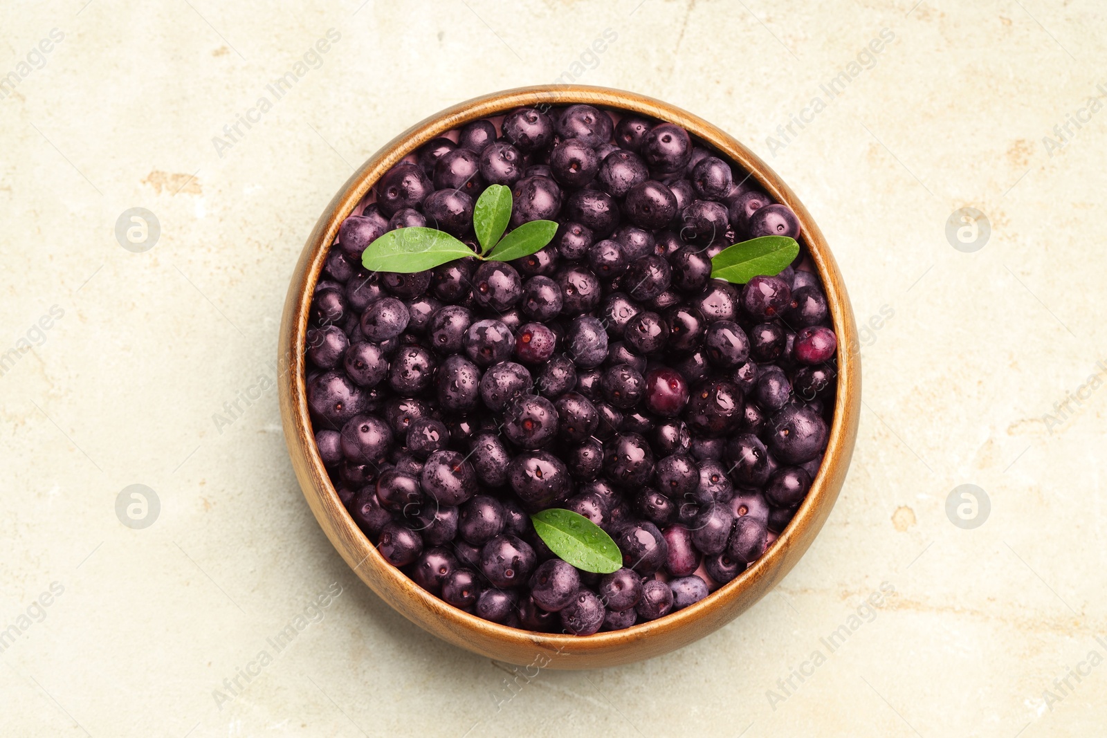 Photo of Ripe acai berries and leaves in bowl on light table, top view