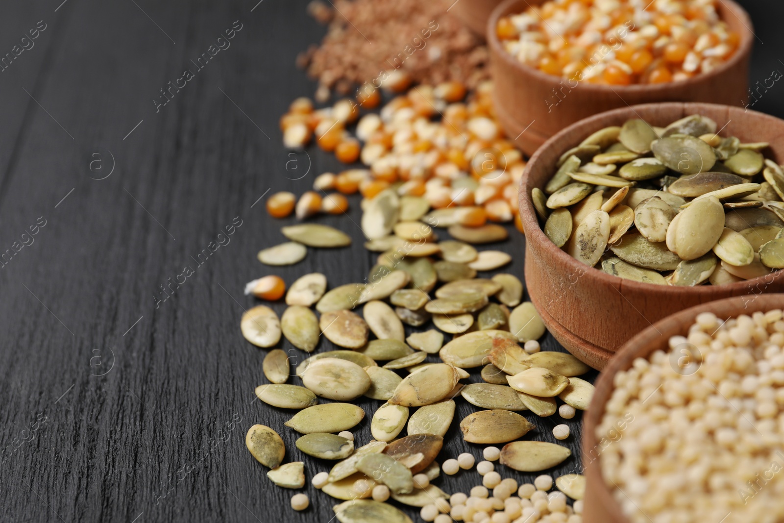 Photo of Different types of seeds and cereals in bowls on black wooden table, closeup. Space for text