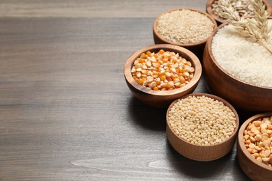 Photo of Different types of cereals in bowls on wooden table, closeup. Space for text