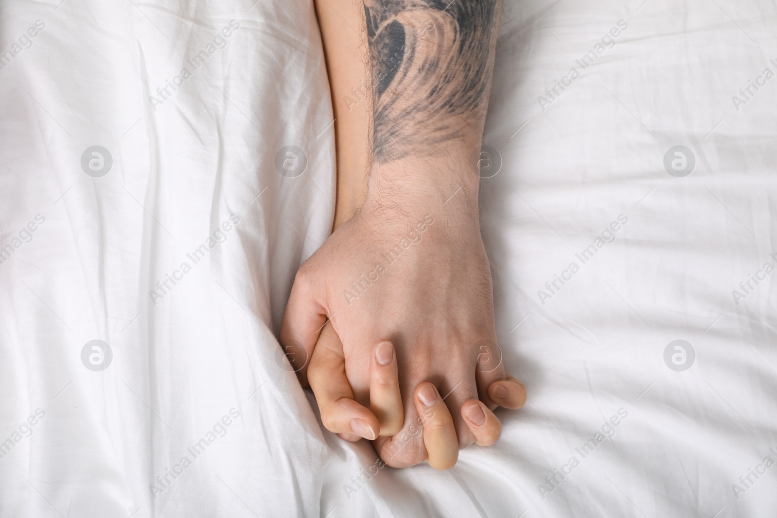 Photo of Lovely couple holding hands in bed, top view