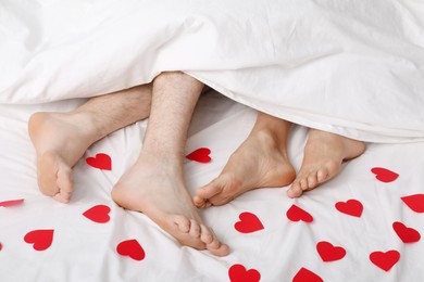 Photo of Couple lying in bed with red paper hearts, closeup