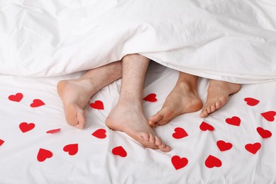 Photo of Couple lying in bed with red paper hearts, closeup