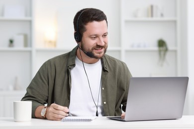 Interpreter in headset taking notes while having video chat via laptop at white table indoors