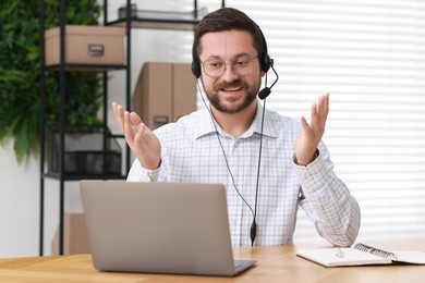 Interpreter in headset having video chat via laptop at wooden table indoors