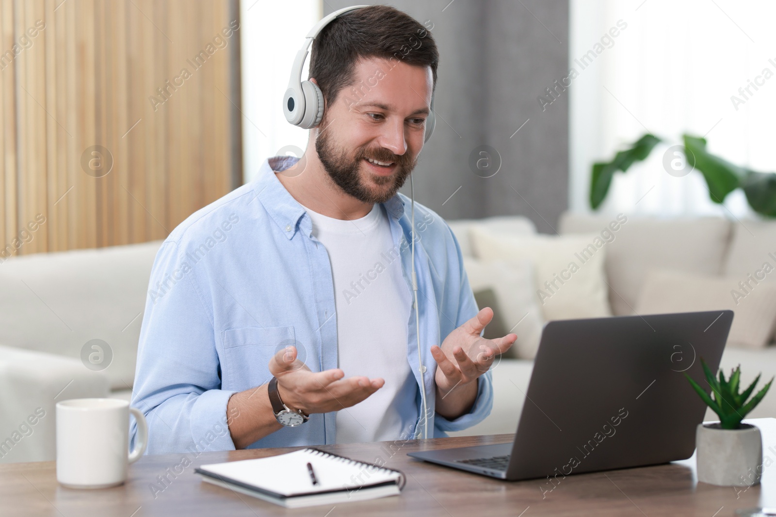 Photo of Interpreter in headphones having video chat via laptop at wooden table indoors