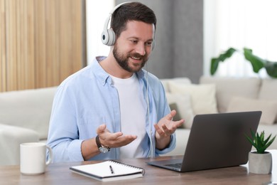 Interpreter in headphones having video chat via laptop at wooden table indoors