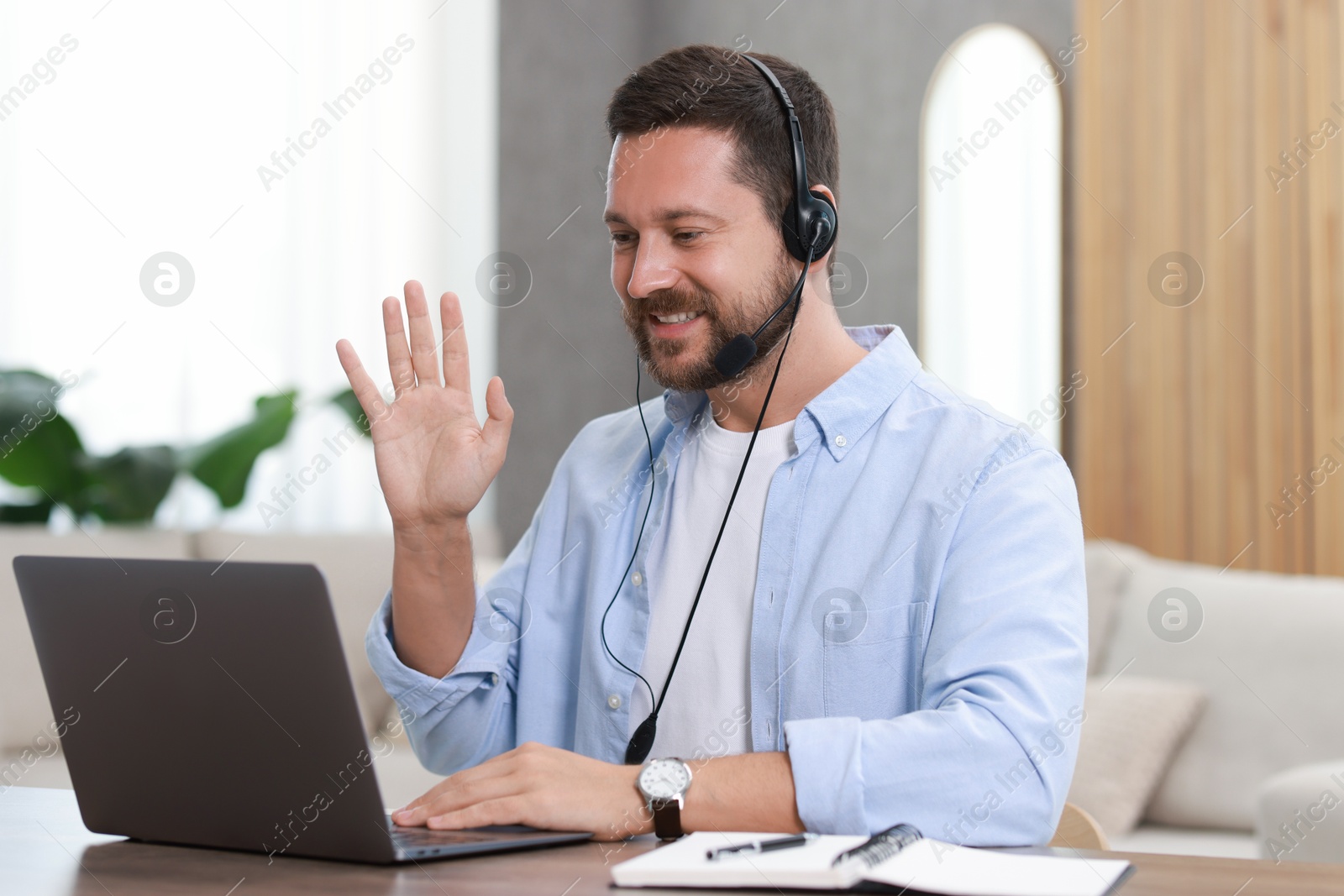 Photo of Interpreter in headset having video chat via laptop at wooden table indoors