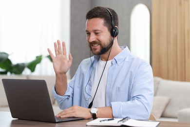 Interpreter in headset having video chat via laptop at wooden table indoors