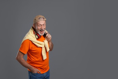 Portrait of happy senior man with headphones on grey background. Space for text