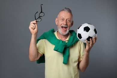 Portrait of emotional senior man with soccer ball on grey background