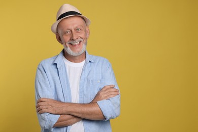 Portrait of happy senior man with crossed arms on yellow background. Space for text