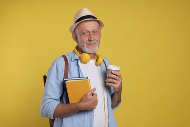 Photo of Portrait of handsome senior man with books and paper cup on yellow background