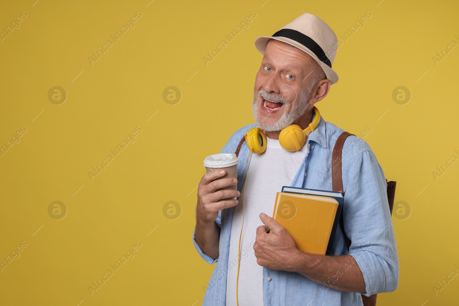 Photo of Portrait of happy senior man with books and paper cup on yellow background. Space for text