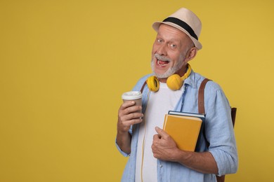 Portrait of happy senior man with books and paper cup on yellow background. Space for text