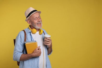 Portrait of happy senior man with books and paper cup on yellow background. Space for text