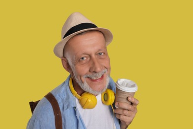 Portrait of happy senior man with paper cup on yellow background