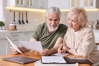 Pension savings. Senior couple planning budget at wooden table indoors