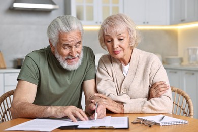 Pension savings. Senior couple planning budget at wooden table indoors