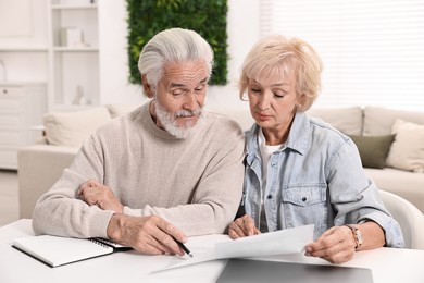 Photo of Pension savings. Senior couple planning budget at white table indoors