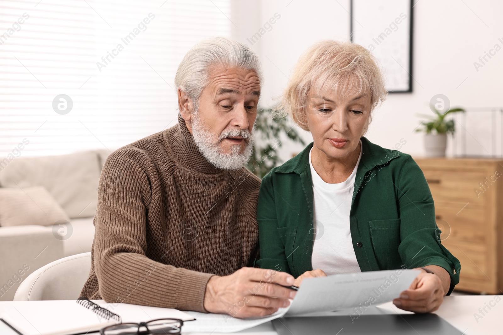 Photo of Pension savings. Senior couple planning budget at white table indoors