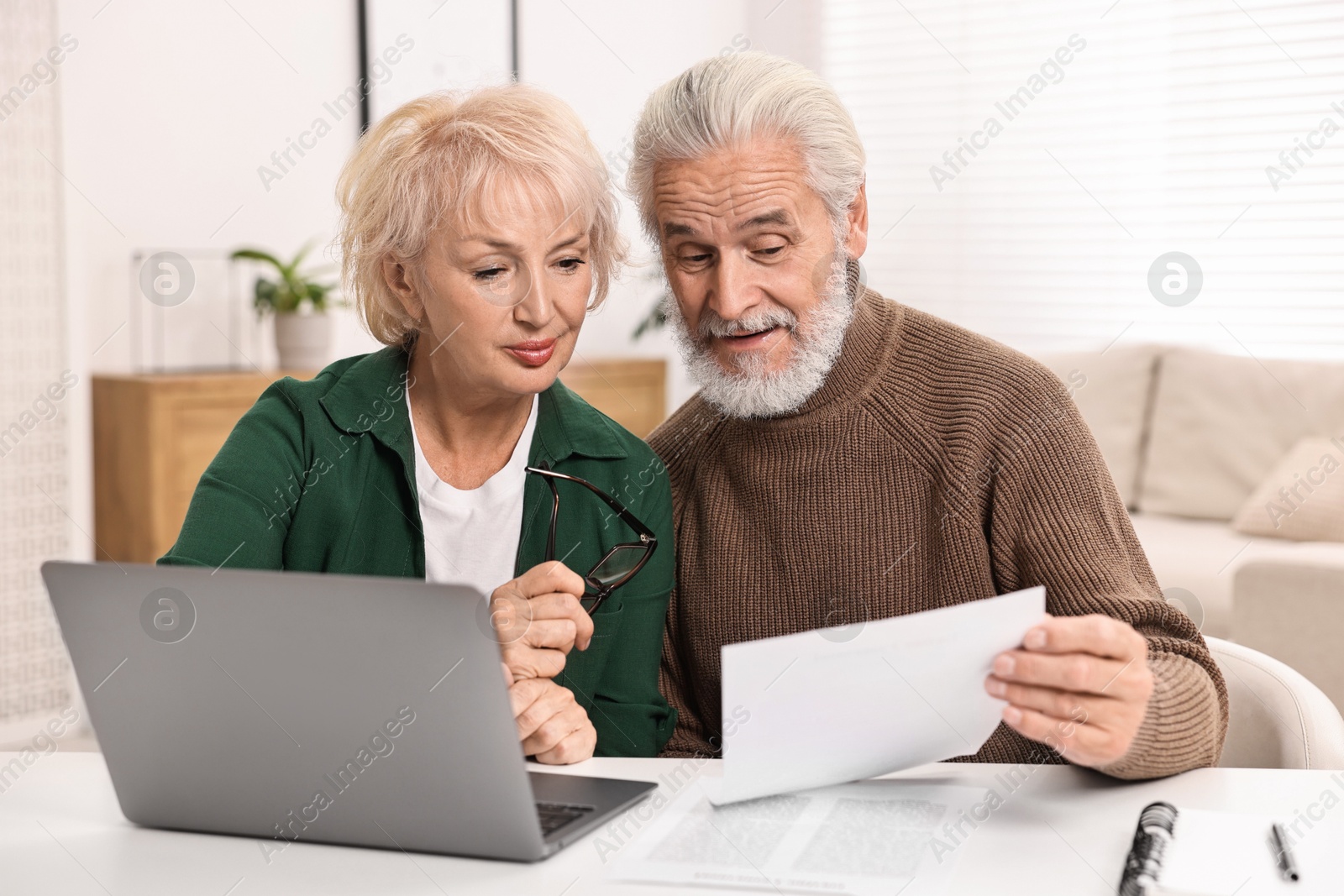 Photo of Pension savings. Senior couple planning budget at white table indoors