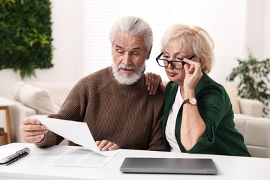 Photo of Pension savings. Senior couple planning budget at white table indoors