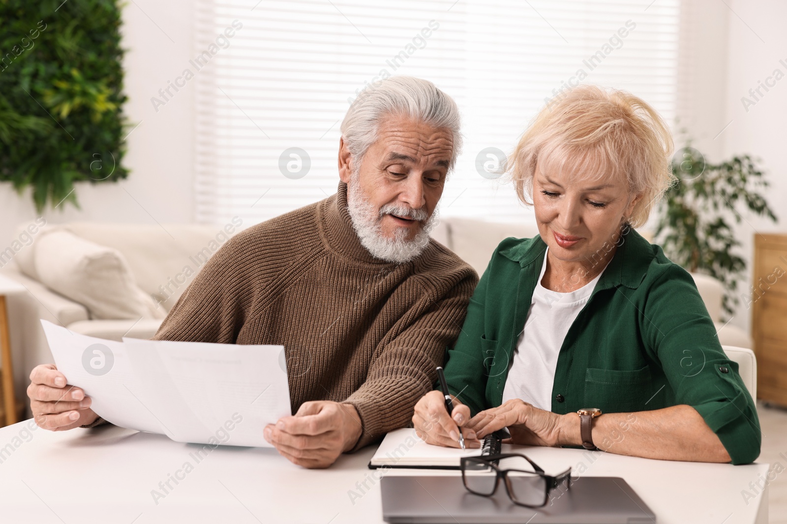 Photo of Pension savings. Senior couple planning budget at white table indoors