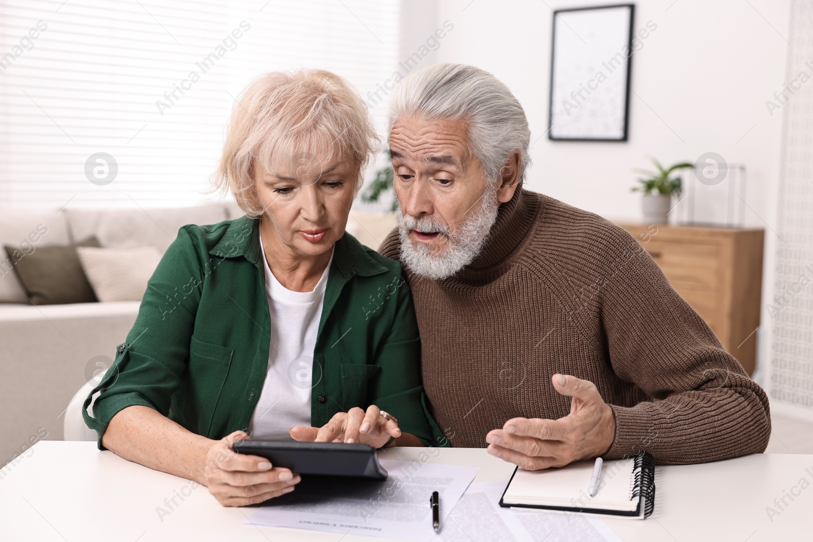 Photo of Pension savings. Senior couple planning budget at white table indoors