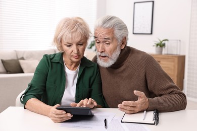 Photo of Pension savings. Senior couple planning budget at white table indoors