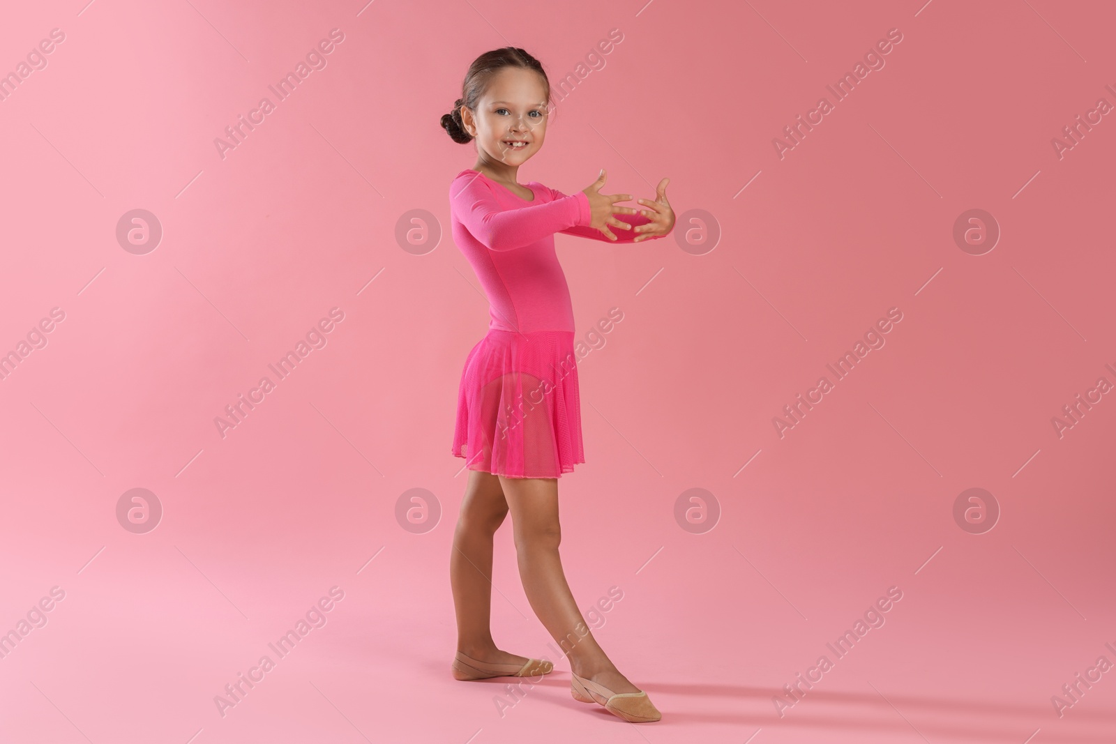 Photo of Little ballerina practicing dance moves on pink background